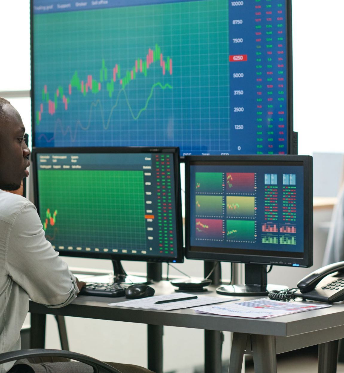 African American and Caucasian men in formalwear sitting in front of computer monitors analyzing currency stats